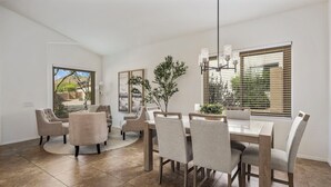 A dining area with a wooden table and chairs, a potted plant, and a view of the outdoors through large windows.