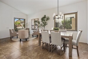 A dining area with a wooden table and chairs, a potted plant, and a view of the outdoors through large windows. - Luxe Desert Oasis w/Pool + Mtn Views (Mesa)