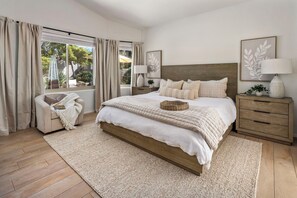 A bedroom with a large bed, wooden headboard, two bedside tables, a window with curtains, and a view of the outdoors. - Luxe Desert Oasis w/Pool + Mtn Views (Mesa)