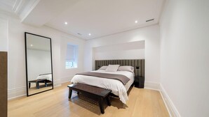 Ein modernes Schlafzimmer mit einem großen Bett, einer Bank, einem Spiegel und einem Fenster.