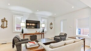 Ein Wohnzimmer mit einer Couch, Sesseln, einem Couchtisch, einem Fernseher und dekorativen Wandleuchten.