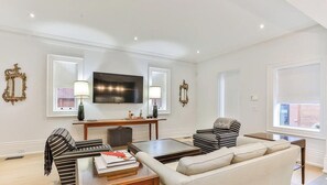 A living room with a sofa, armchairs, a coffee table, a TV, and decorative wall sconces.
