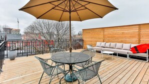 Eine Dachterrasse mit Tisch, Stühlen, einer Sitzecke und einem großen Sonnenschirm.