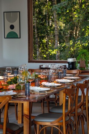 Taula de dinar preparada amb vasos de vi, plats i coberts, amb vista a arbres a través d'una finestra gran.