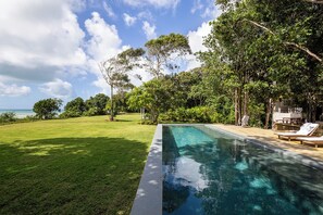 Una piscina amb vistes clares a l'oceà, envoltada de vegetació exuberant i un jardí ben cuidat.