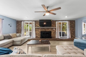 Ein Wohnzimmer mit Ecksofa, Couchtisch, Kamin und Fernseher an einer Ziegelwand.