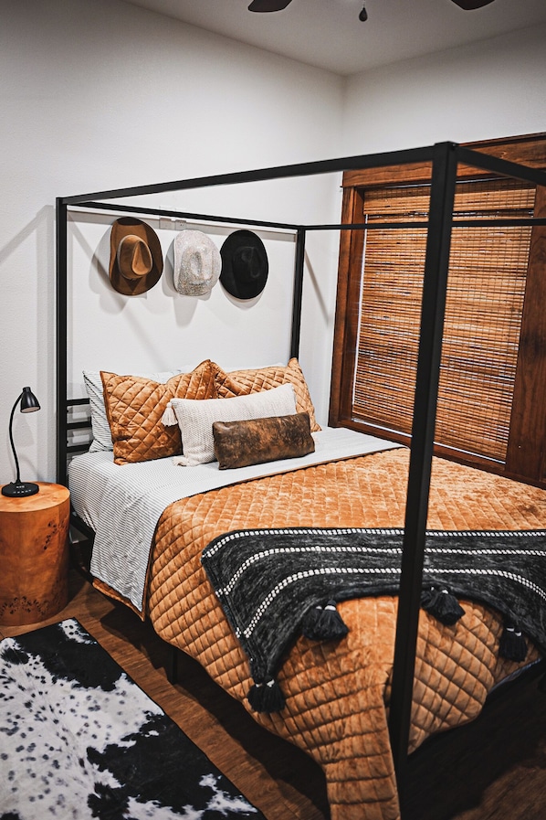 A four-poster bed with a quilted orange bedspread, a wooden headboard, and a bedside table with a lamp.