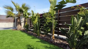 Un jardin bien entretenu, agrémenté de diverses plantes tropicales, une pelouse soigneusement taillée et une clôture en bois.