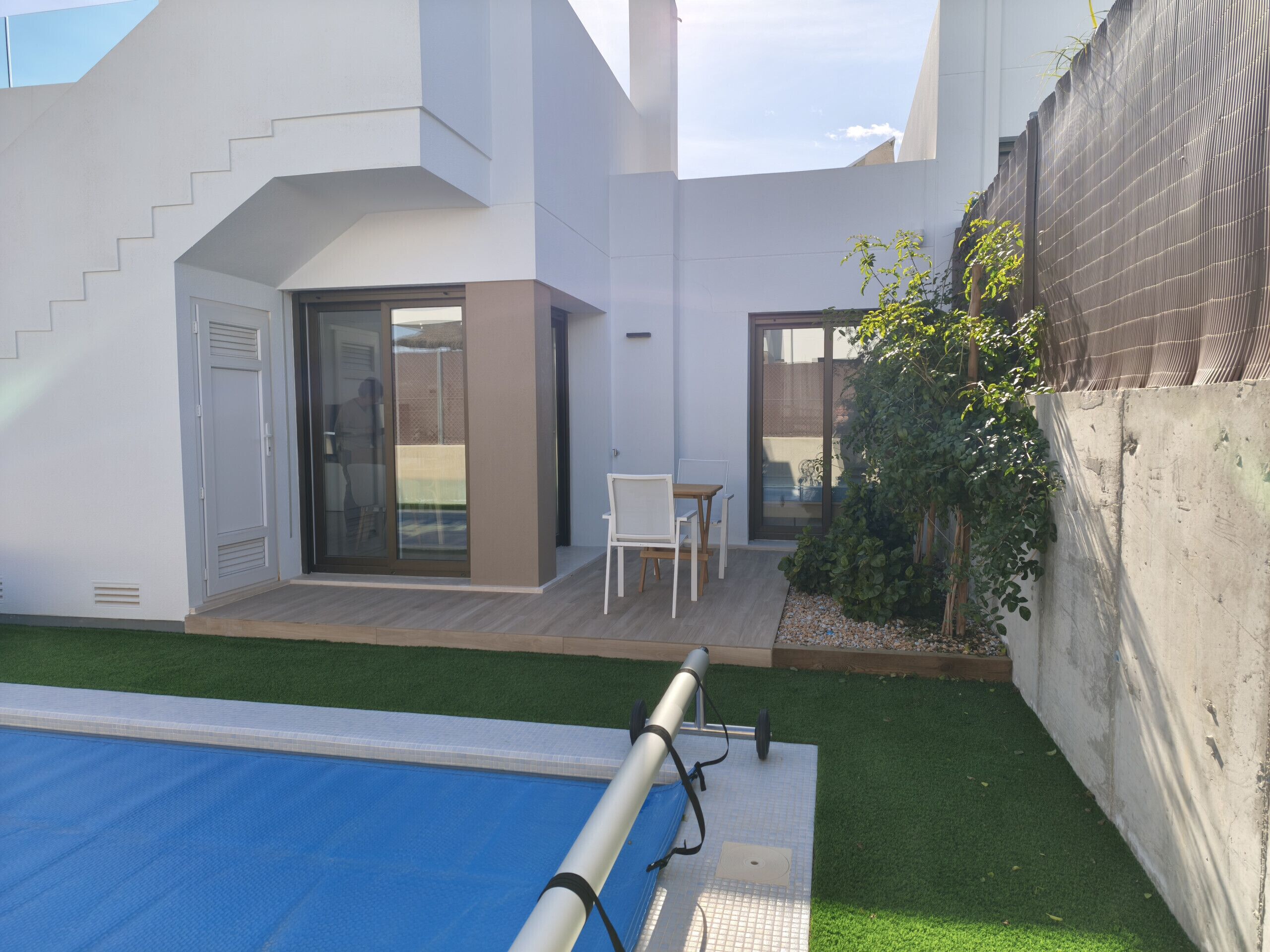 Un moderno edificio residencial con piscina, un patio con sillas y un pequeño jardín.