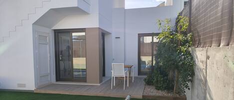 Un moderno edificio residencial con piscina, un patio con sillas y un pequeño jardín.