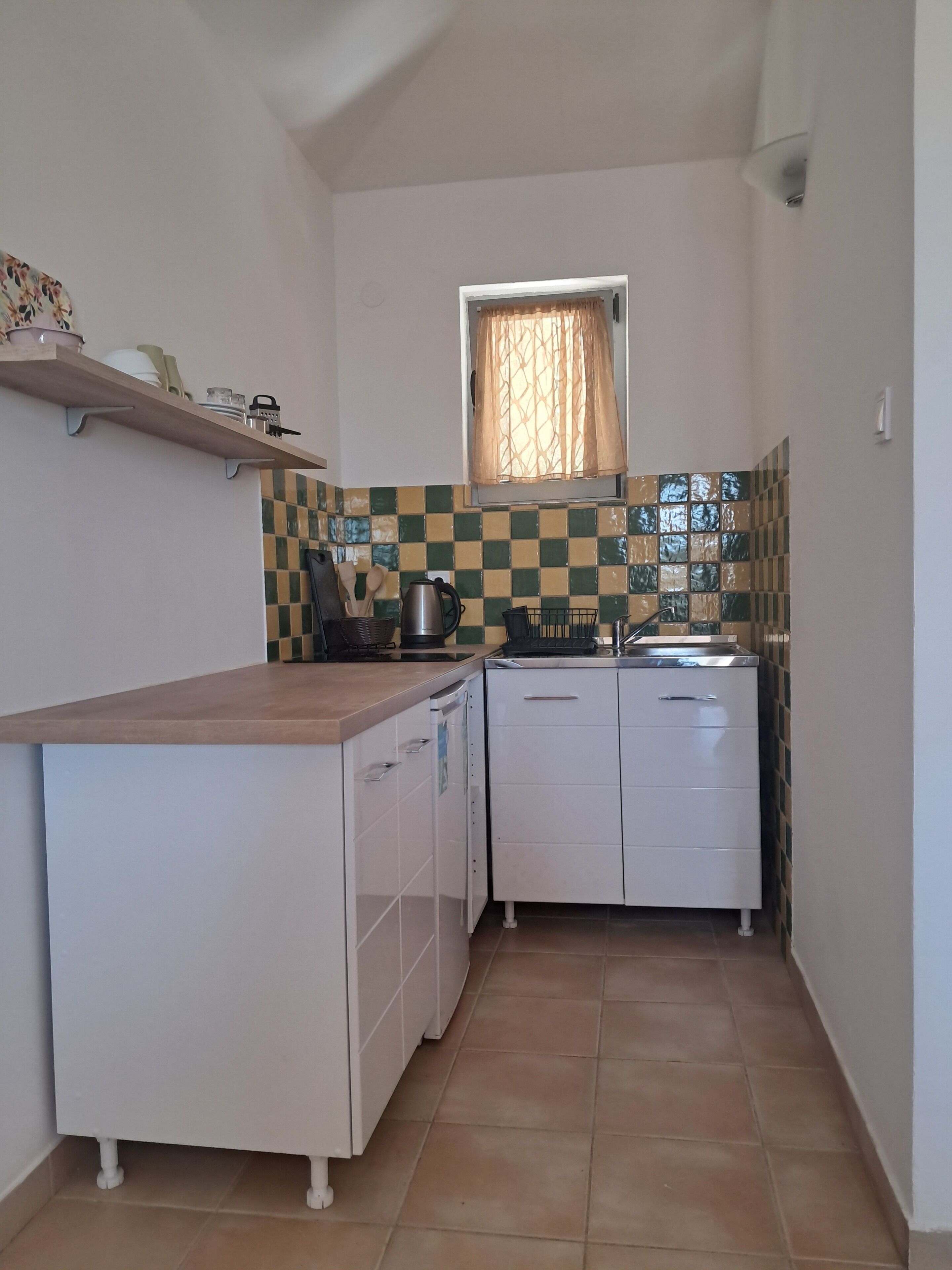 A compact kitchen with a tiled backsplash, a window with a curtain, and a built-in dishwasher.
