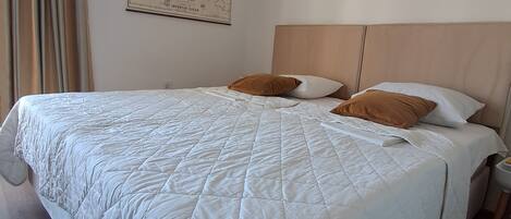 A neatly made bed with a quilted white duvet, a wooden headboard, and a wall map.
