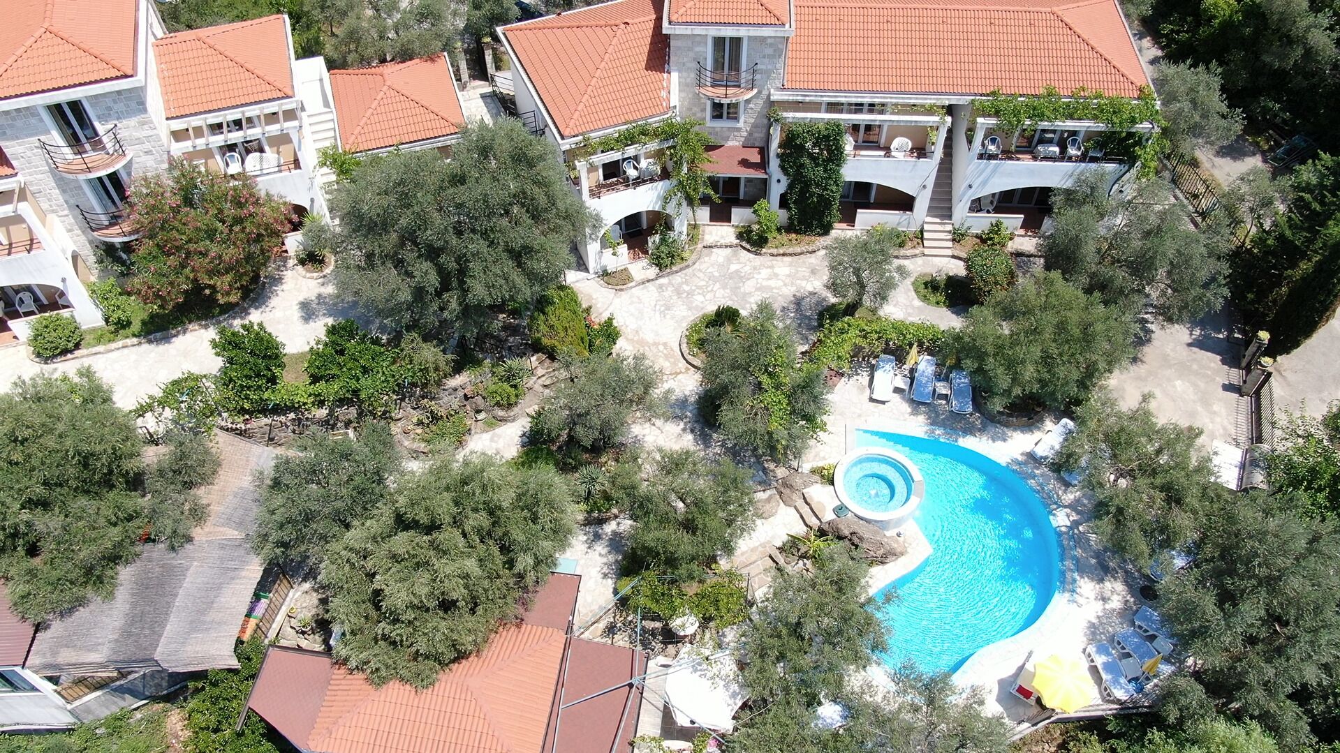 An aerial view of a residential area with a swimming pool, multiple houses, and surrounding greenery.