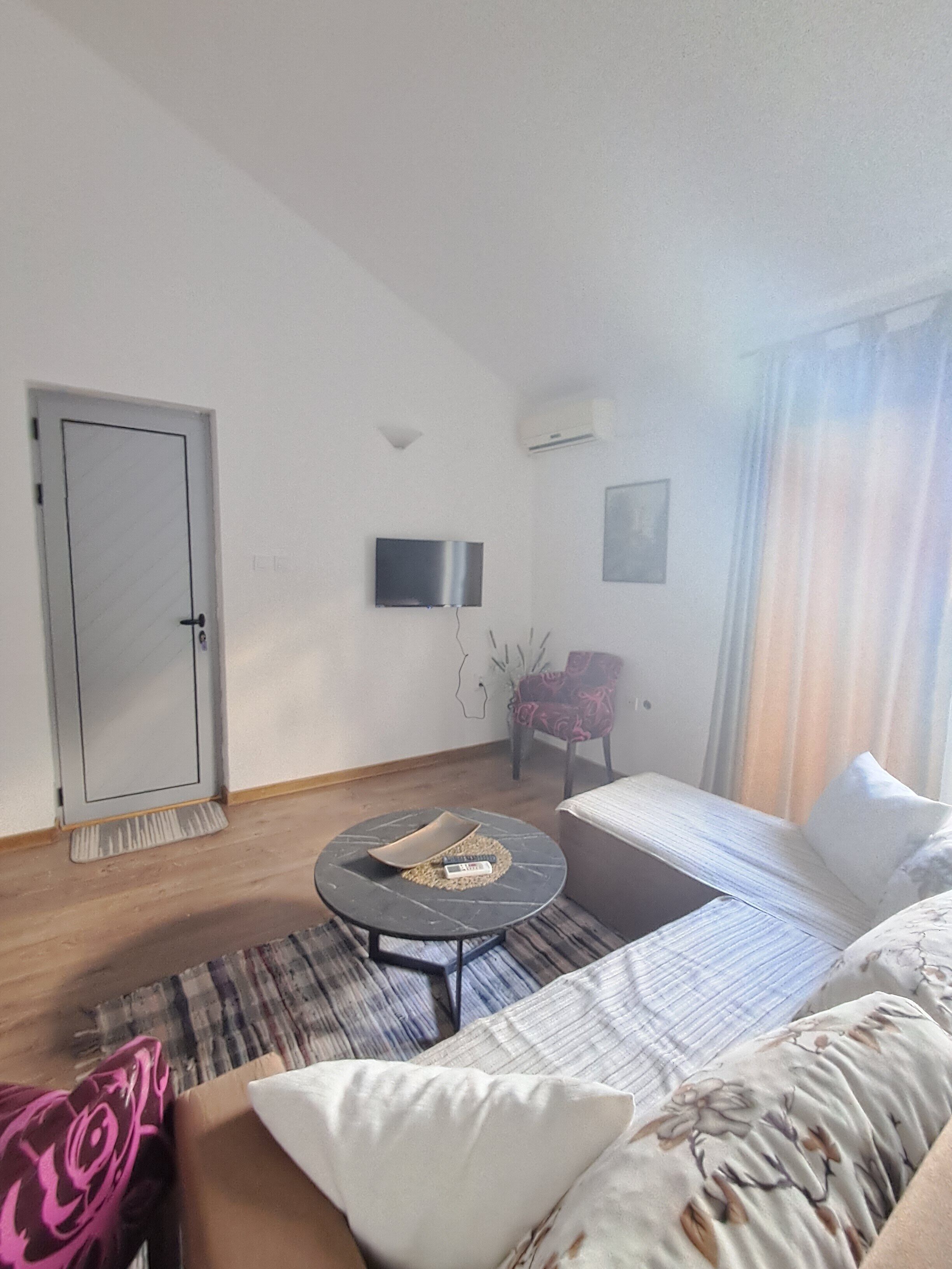 A modern living room with a sofa, a small round table, a TV, and a door.