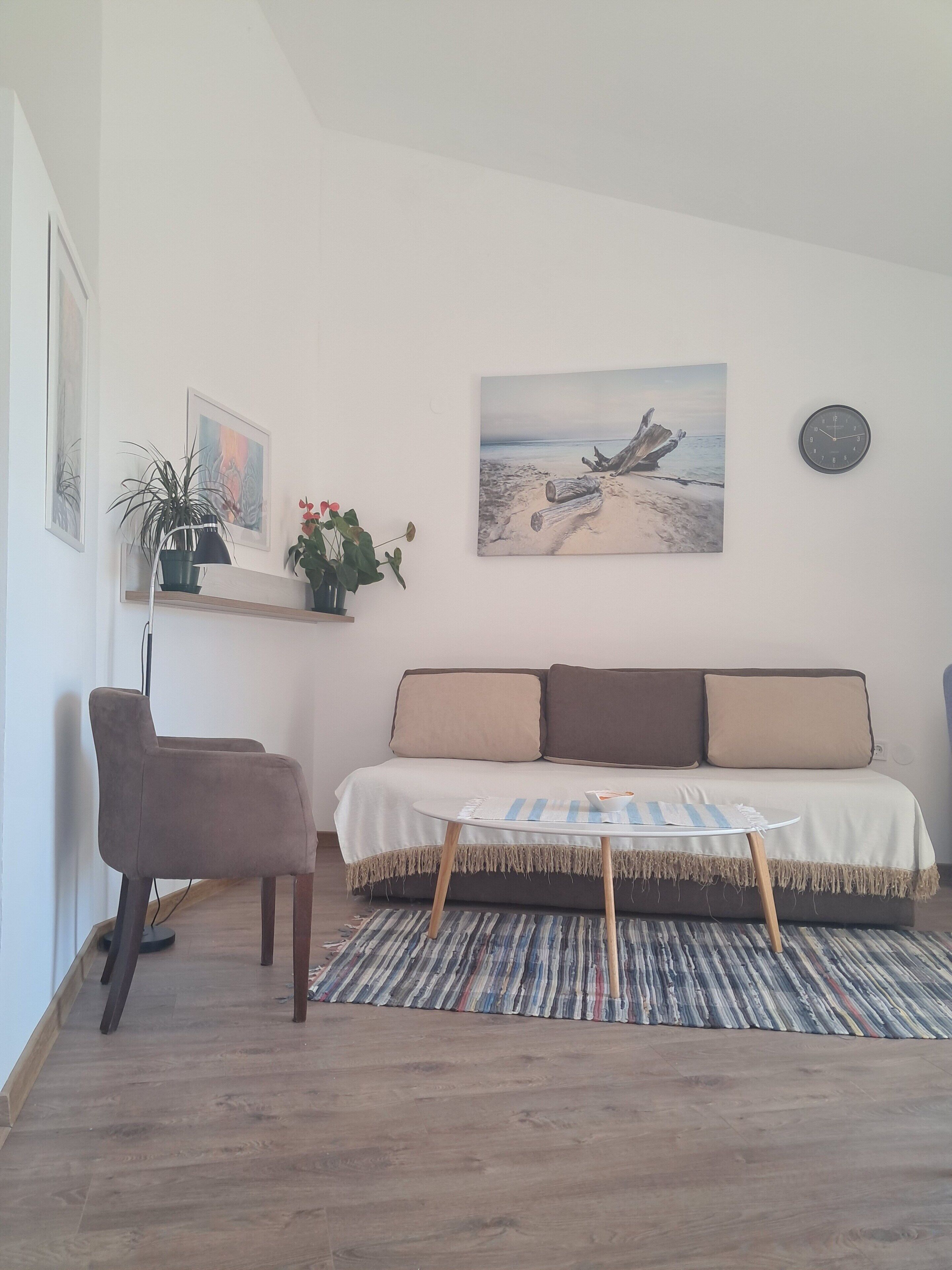 Un salon comprenant un canapé, un fauteuil, une petite table, une horloge et des œuvres d’art accrochées au mur.