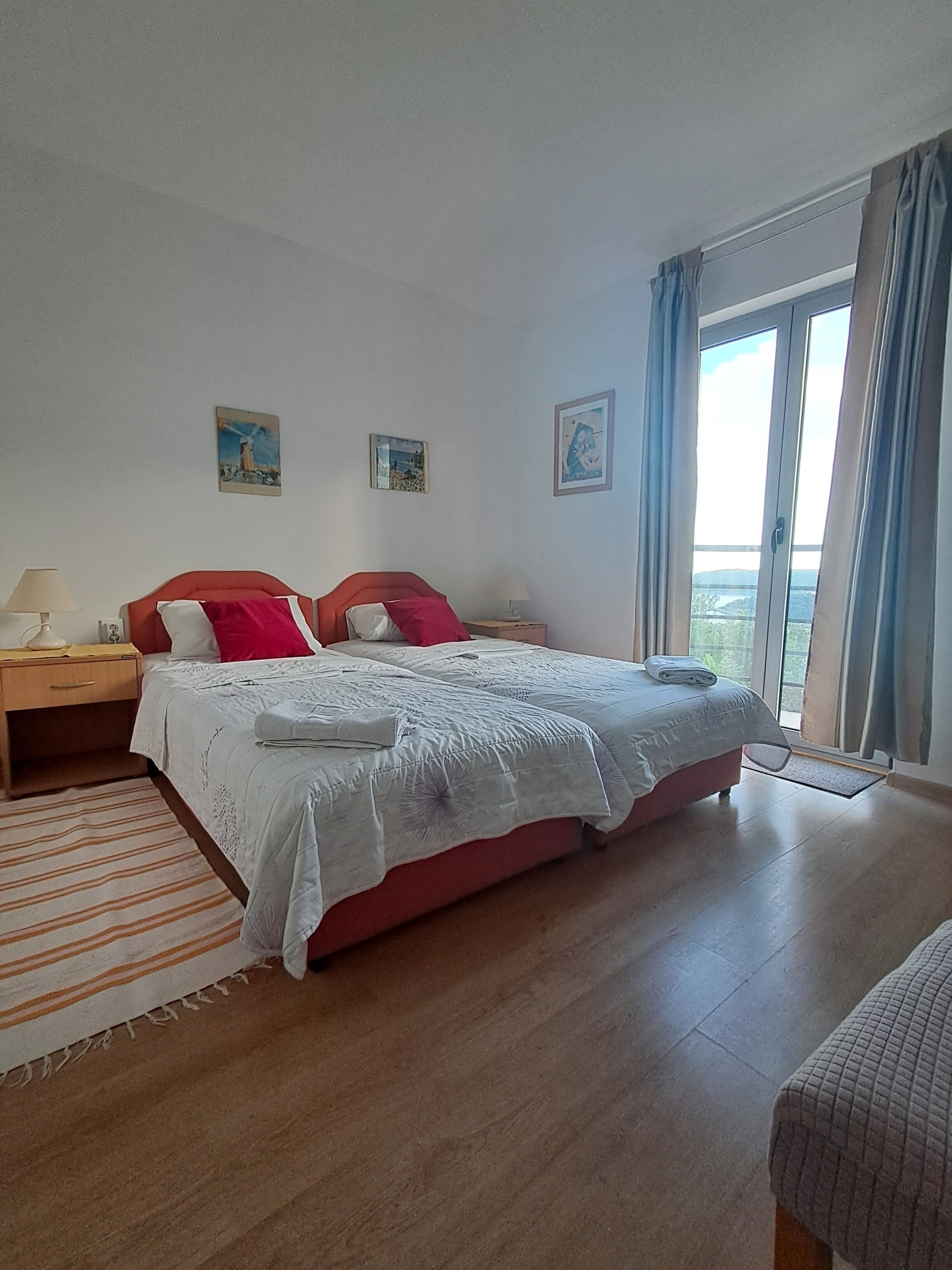 A bedroom with a bed, two bedside tables, a window with curtains, and three wall-mounted pictures.