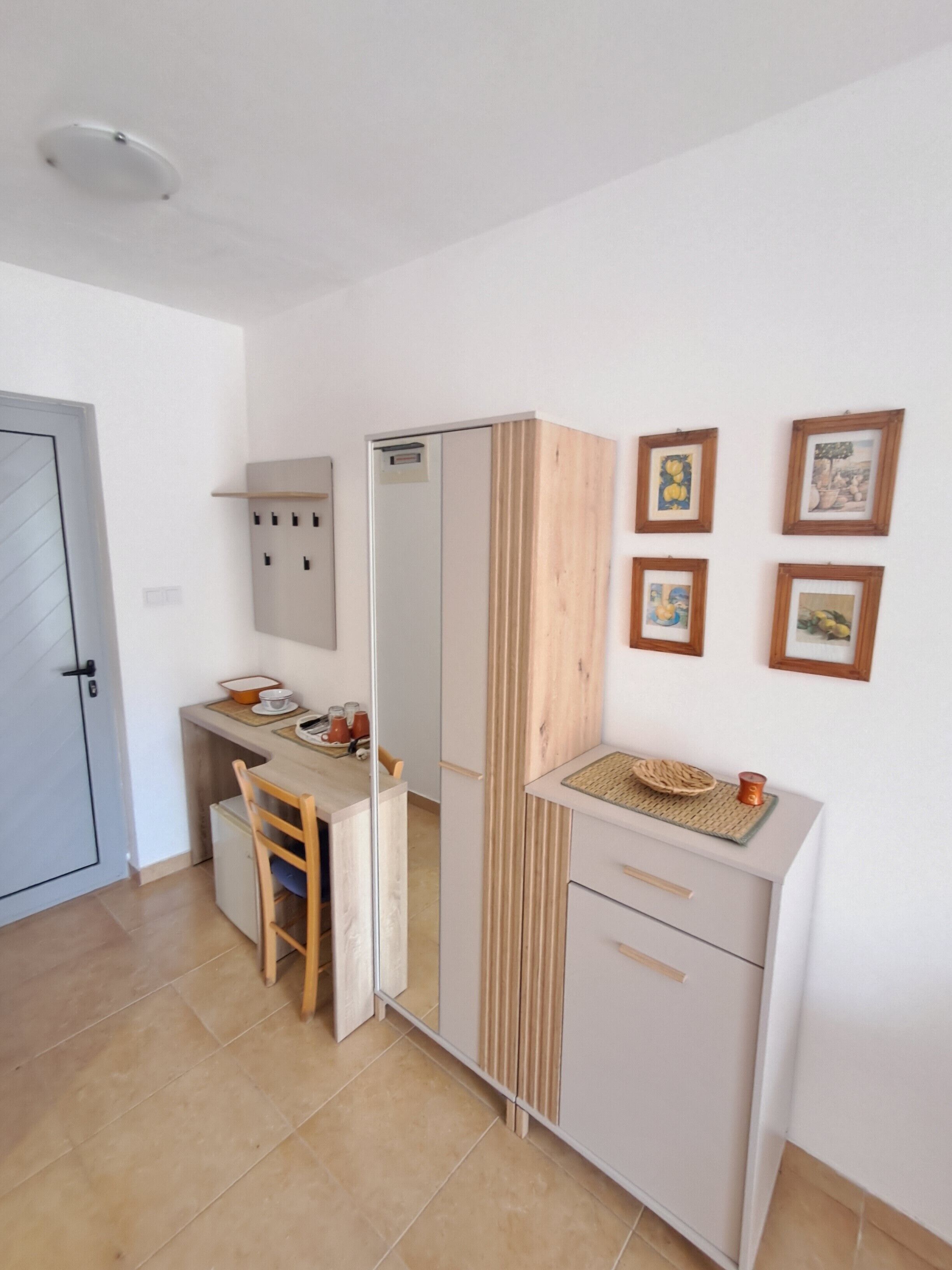 A compact kitchen with a wooden chair, a small refrigerator, and a cabinet with a mirror.