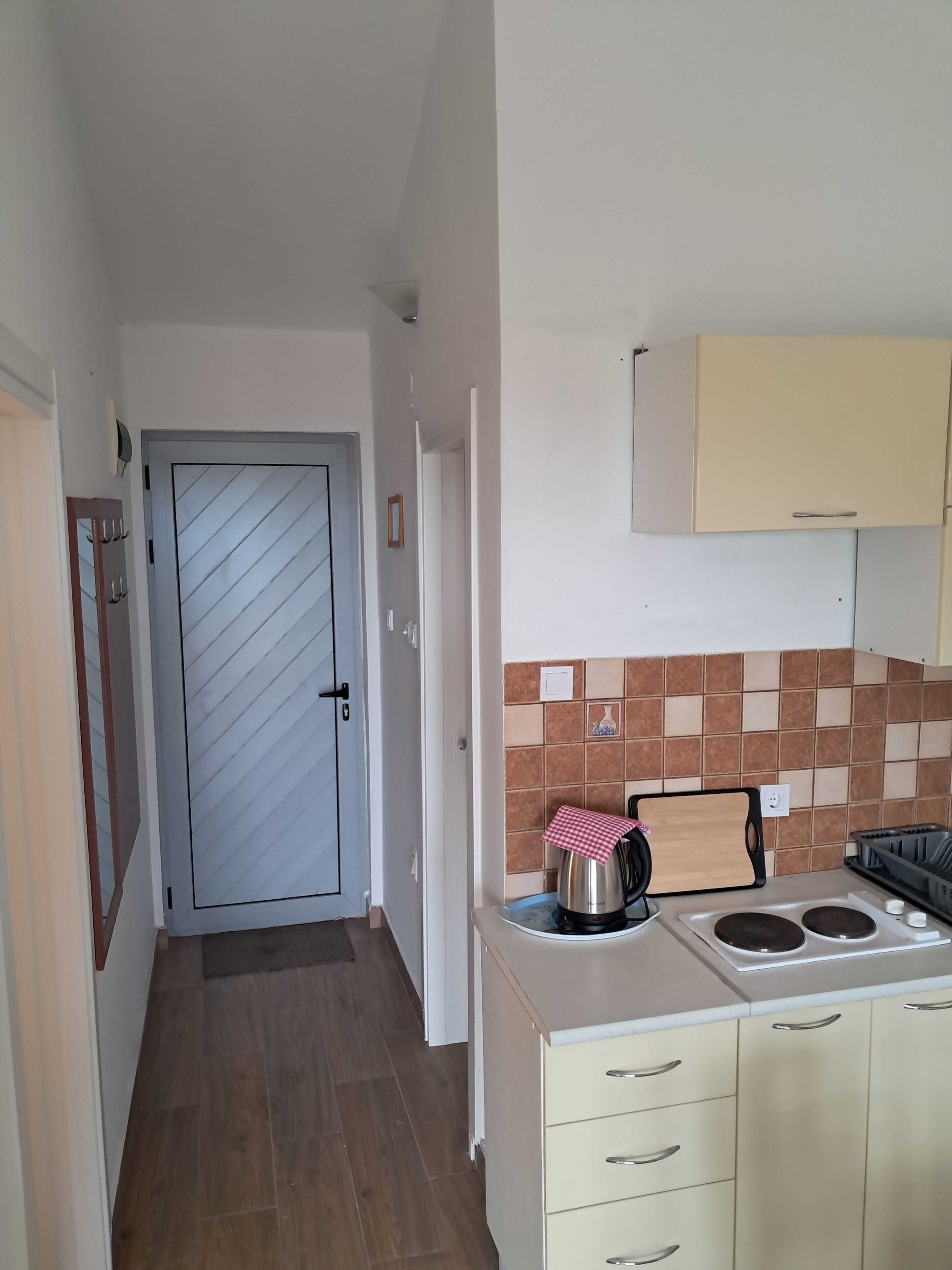 A narrow hallway leading to a kitchen with a tiled backsplash, a stove, and a sink.