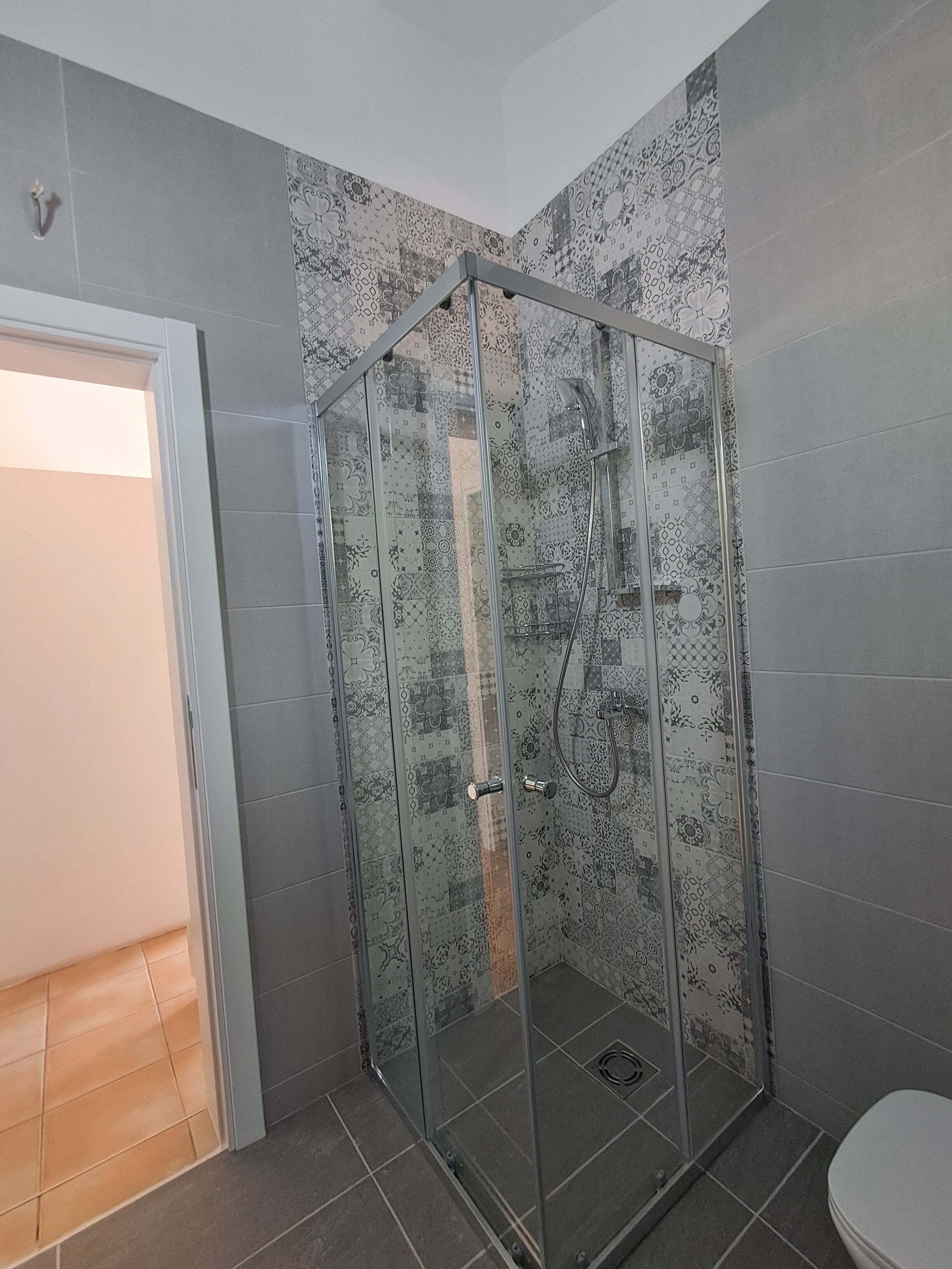 A glass-enclosed shower with patterned tiles, a white door, and a tiled floor.