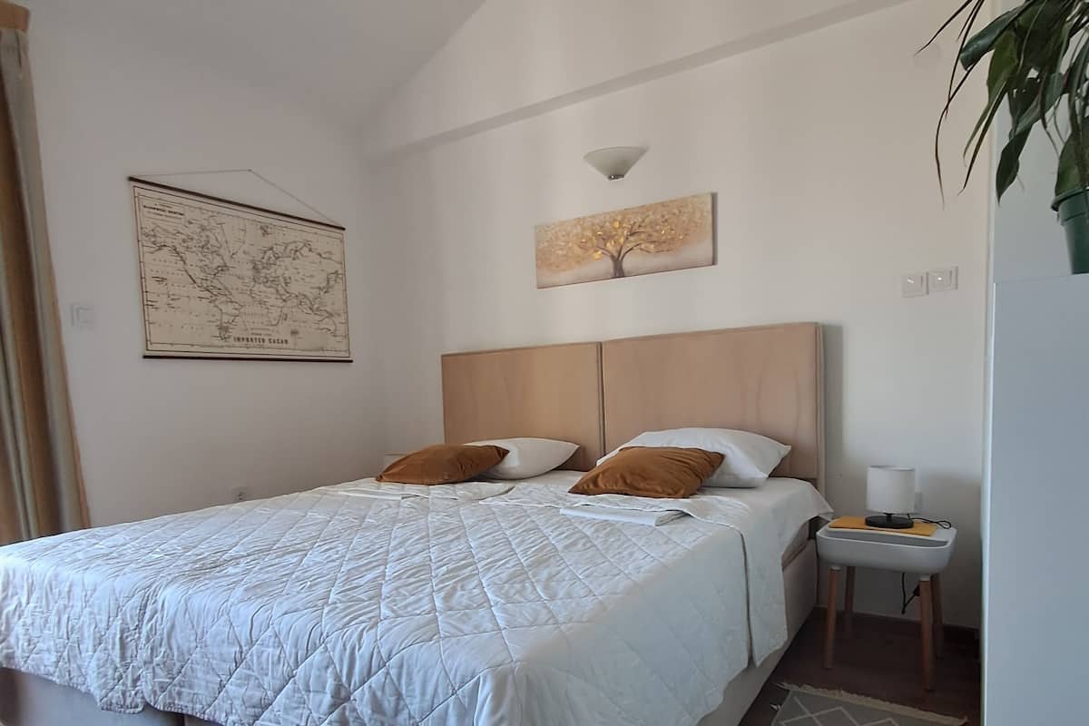 A bedroom with a bed, a nightstand, a lamp, a map, and a painting on the wall.