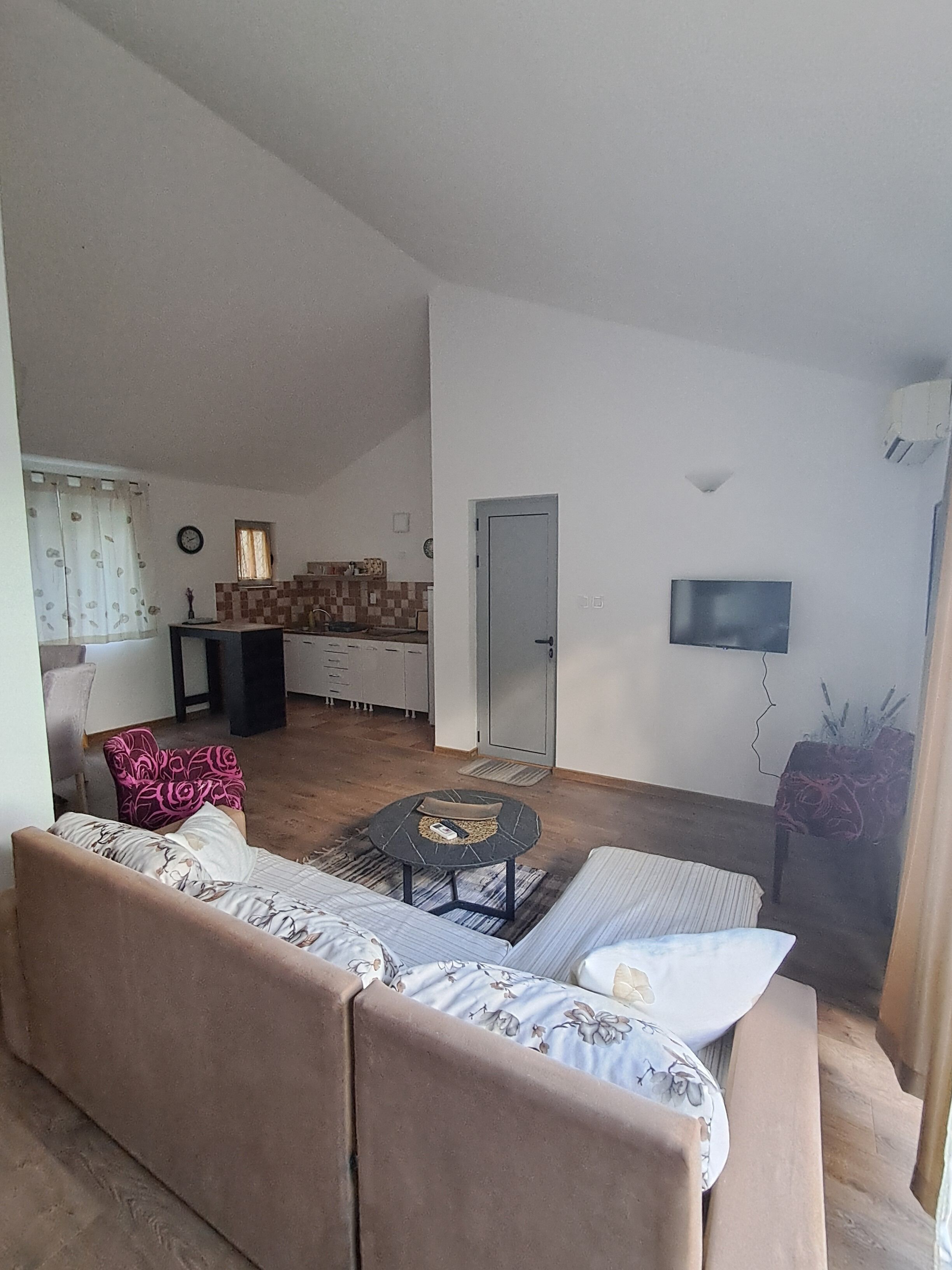 A living room with a sofa, a coffee table, a TV, and a kitchen in the background.