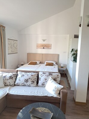 A hotel room with a bed, a sofa, a small table, a map, and a plant. - Resort Maslinjak (Bečići)