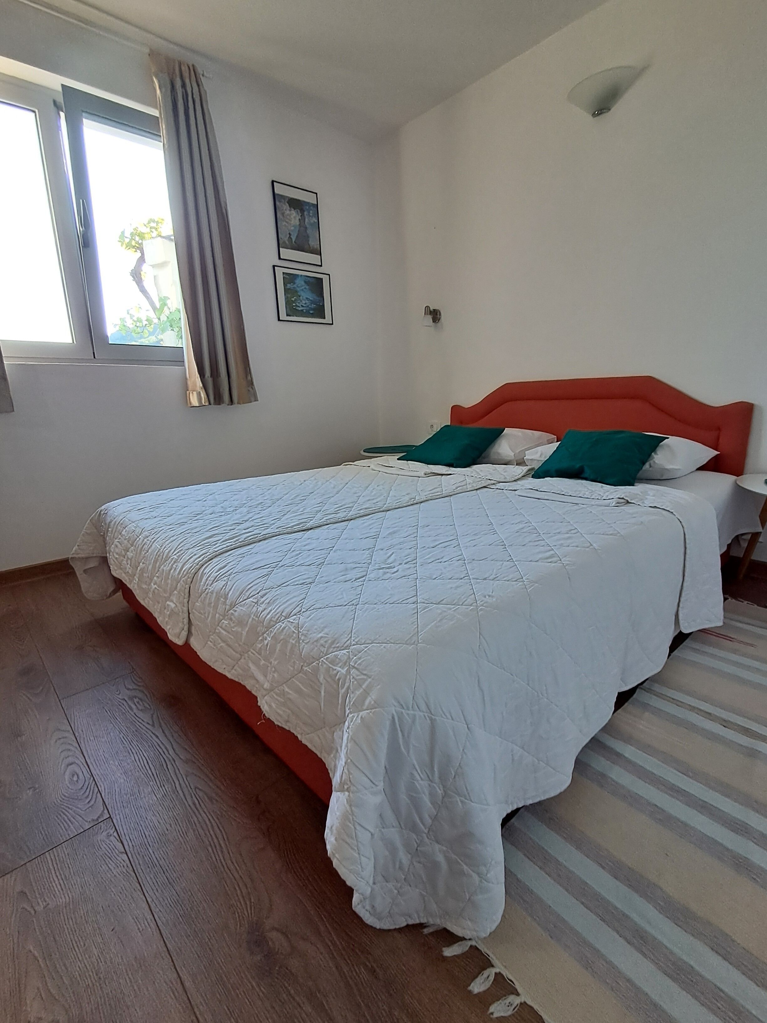 A bedroom with a bed, a window with curtains, a wall-mounted light, and a door.