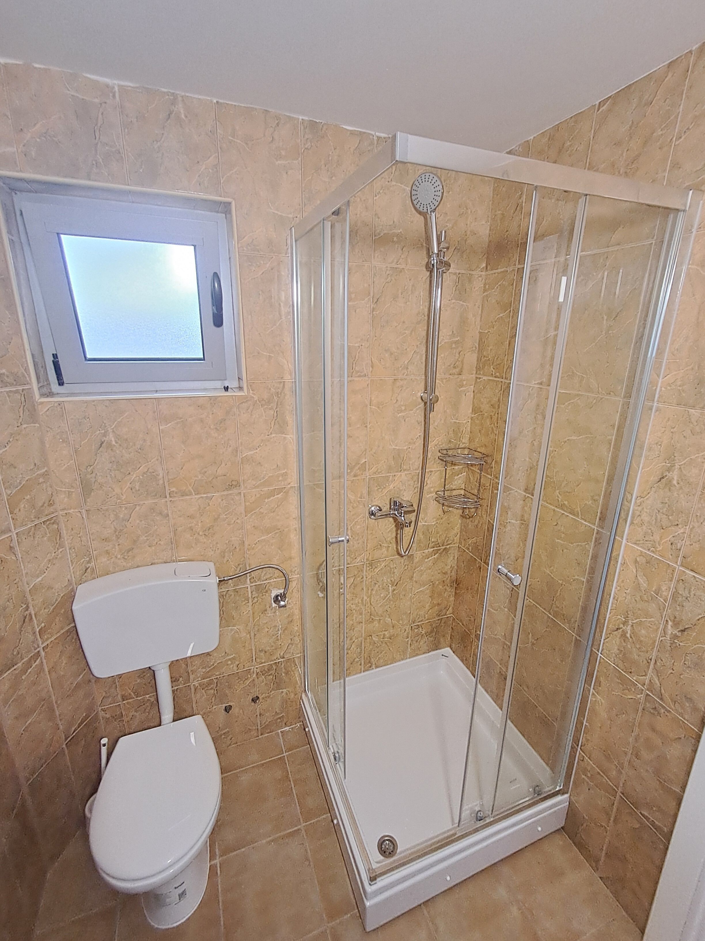A bathroom with a shower, toilet, and a small window.
