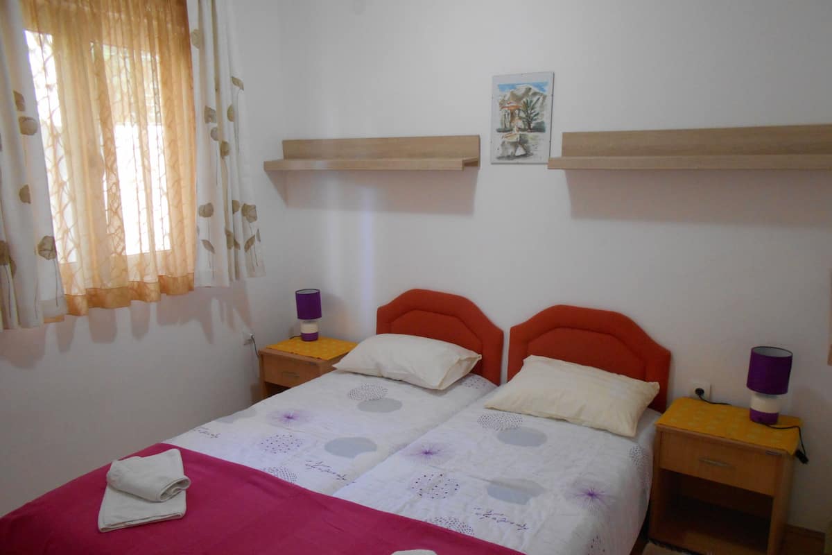 A bedroom with a bed, two nightstands, a window with curtains, and a wall-mounted shelf.