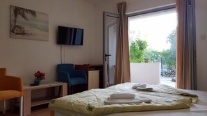 Ein Hotelzimmer mit Bett, Schreibtisch, Stuhl, Fernseher und einem Balkon mit Vorhängen.
