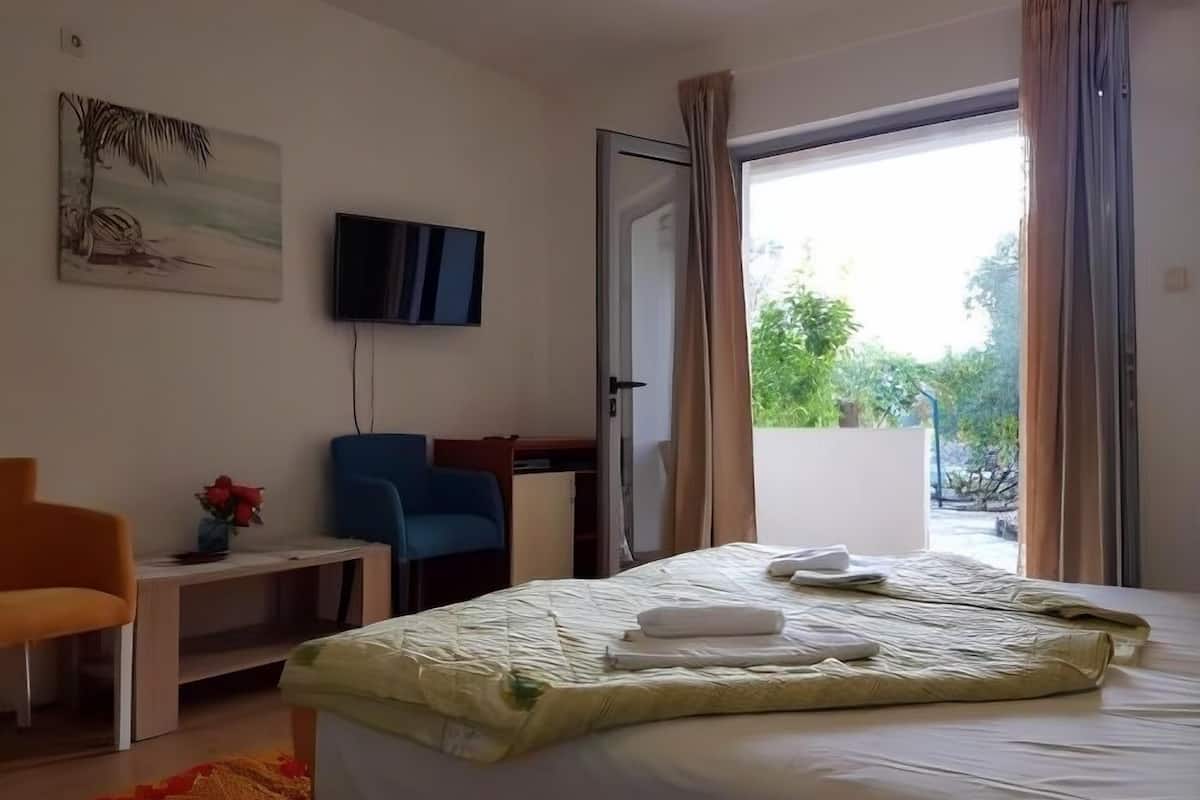 A hotel room with a bed, a desk, a chair, a TV, and a balcony with curtains.