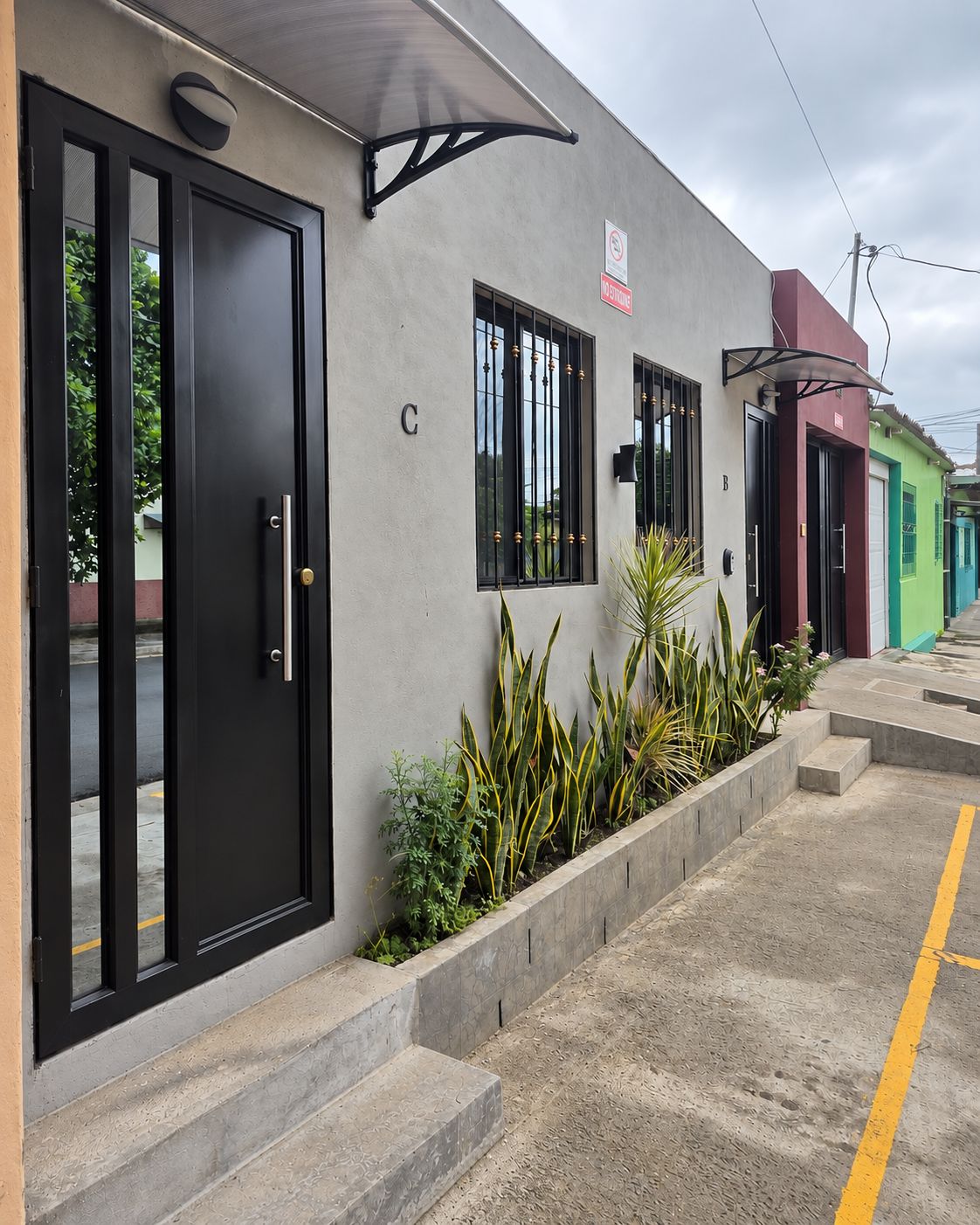 A building with a black door, a window with a metal grill, and a sign indicating no parking.