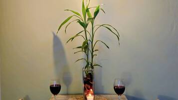 A dining table with two chairs, a candle, a glass vase with a plant, and two glasses of red wine.