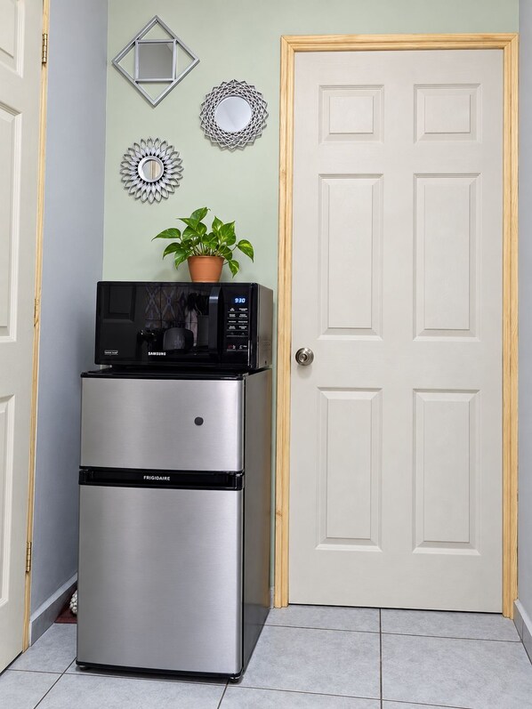 A compact kitchen with a built-in microwave and refrigerator, a potted plant on the microwave, and decorative wall mirrors.