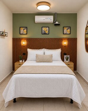 A hotel room with a bed, two bedside tables, a wall-mounted air conditioner, and two wall-mounted lamps.