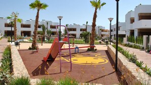 A playground with a slide, swings, and a climbing structure, surrounded by palm trees and modern buildings. - Ground floor Secreto La Zenia (La Zenia)