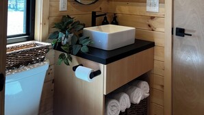 A wooden cabin bathroom with a sink, mirror, and shelves with plants. - “At 84 Ranch, a place to rest, reconnect, and remember what’s real.” (Pagosa Springs)