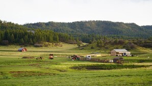 A rural landscape with barns, a tractor, and a fenced area. - “More than a stay-84 Ranch is a connection to the land, the animals, and what truly matters.” (Pagosa Springs)