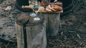 A campfire with a pot, a wooden stool, and a tray with bread and drinks. - “More than a stay-84 Ranch is a connection to the land, the animals, and what truly matters.” (Pagosa Springs)