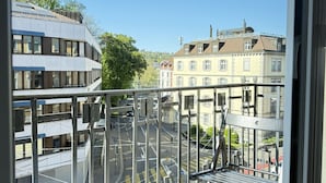 A balcony with a metal railing, a chair, and a view of a city street with buildings and trees. - Stylish studio apartment near the Olma trade fair (St. Gallen)
