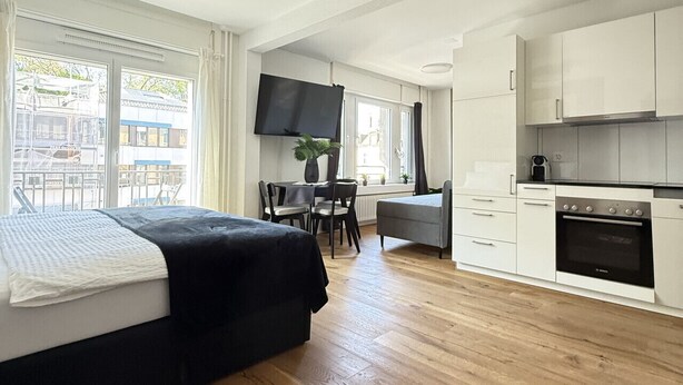 A modern hotel room with a bed, a dining table, chairs, a TV, and a kitchen area. - Stylish studio apartment near the Olma trade fair (St. Gallen)