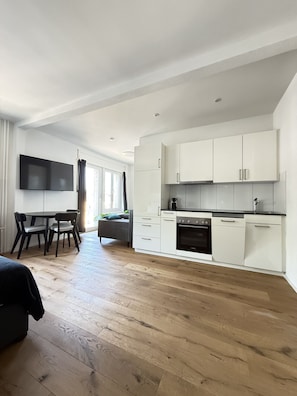 Een moderne keuken met witte kasten, een eethoek met een tafel en stoelen, en een groot raam.