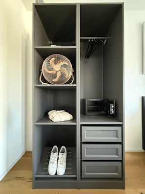 A grey wardrobe with shelves, a fan, a microwave, and a pair of shoes. - Stylish studio apartment near the Olma trade fair (St. Gallen)
