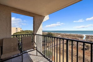 A balcony with two wooden chairs, a view of the beach, and a building in the background. - 3-bed 3 bath ocean front apt, two balconies. Pool, courts, grills, beach access. (Hilton Head Island)