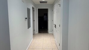 Een gang met lichtgrijze wanden, een betegelde vloer en een plafond met inbouwverlichting.