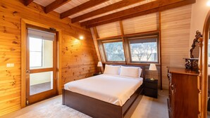 Un dormitorio de cabaña de madera con una cama, dos ventanas, una mesita de noche y un aparador.