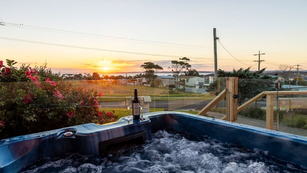 Un jacuzzi con vistas a una puesta de sol, una valla de madera y un área residencial al fondo.