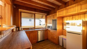 Una cocina de madera con lavavajillas integrado, una ventana con persianas y un refrigerador con calendario.