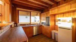 A wooden kitchen with a built-in dishwasher, a window with blinds, and a refrigerator with a calendar.