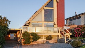 Una casa moderna con un amplio ventanal de vidrio, una terraza de madera y una chimenea de ladrillo rojo.